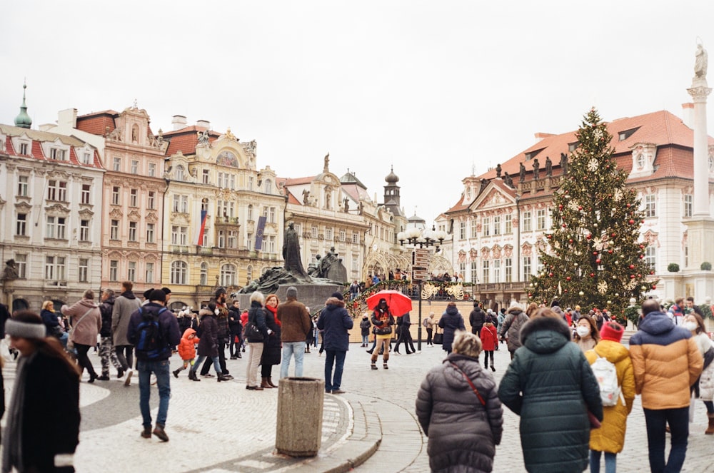 a group of people walking in a plaza with buildings in the background with Old Town Square in the background