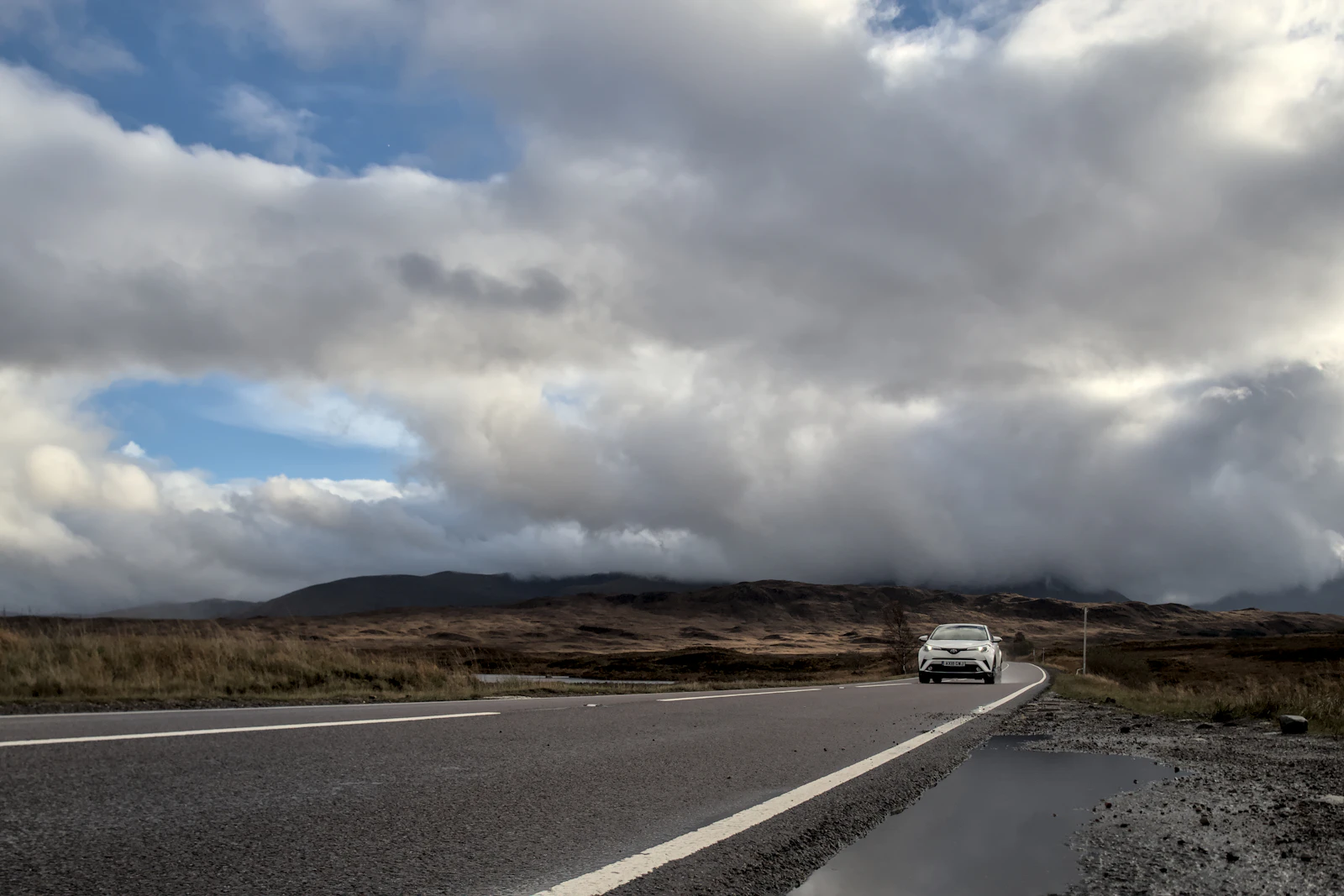 A car travels through the Scottish Highlands on a narrow road