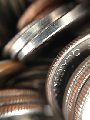 A close-up view of a stack of coins, showcasing their metallic texture and engraved edges. The focus is on the rims and detailed engravings, with the background coins slightly out of focus.