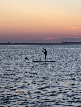 Sunrise over the calm sea with a person standing on a SUP board near the beach in Trójmiasto.