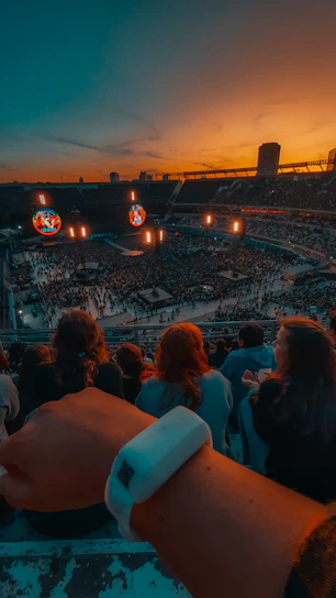 A vibrant crowd gathered in a football stadium at sunset, sharing food and music.