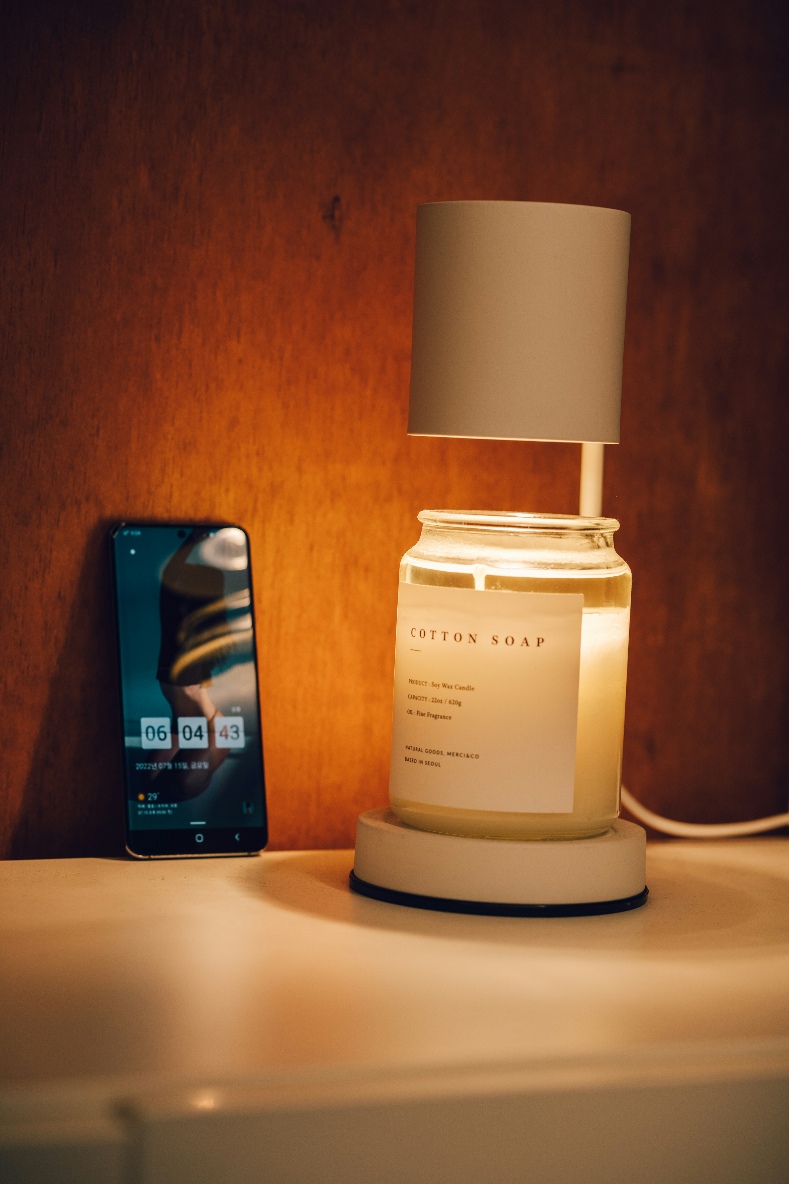 A soy wax candle rests on a warmer beside a smartphone.