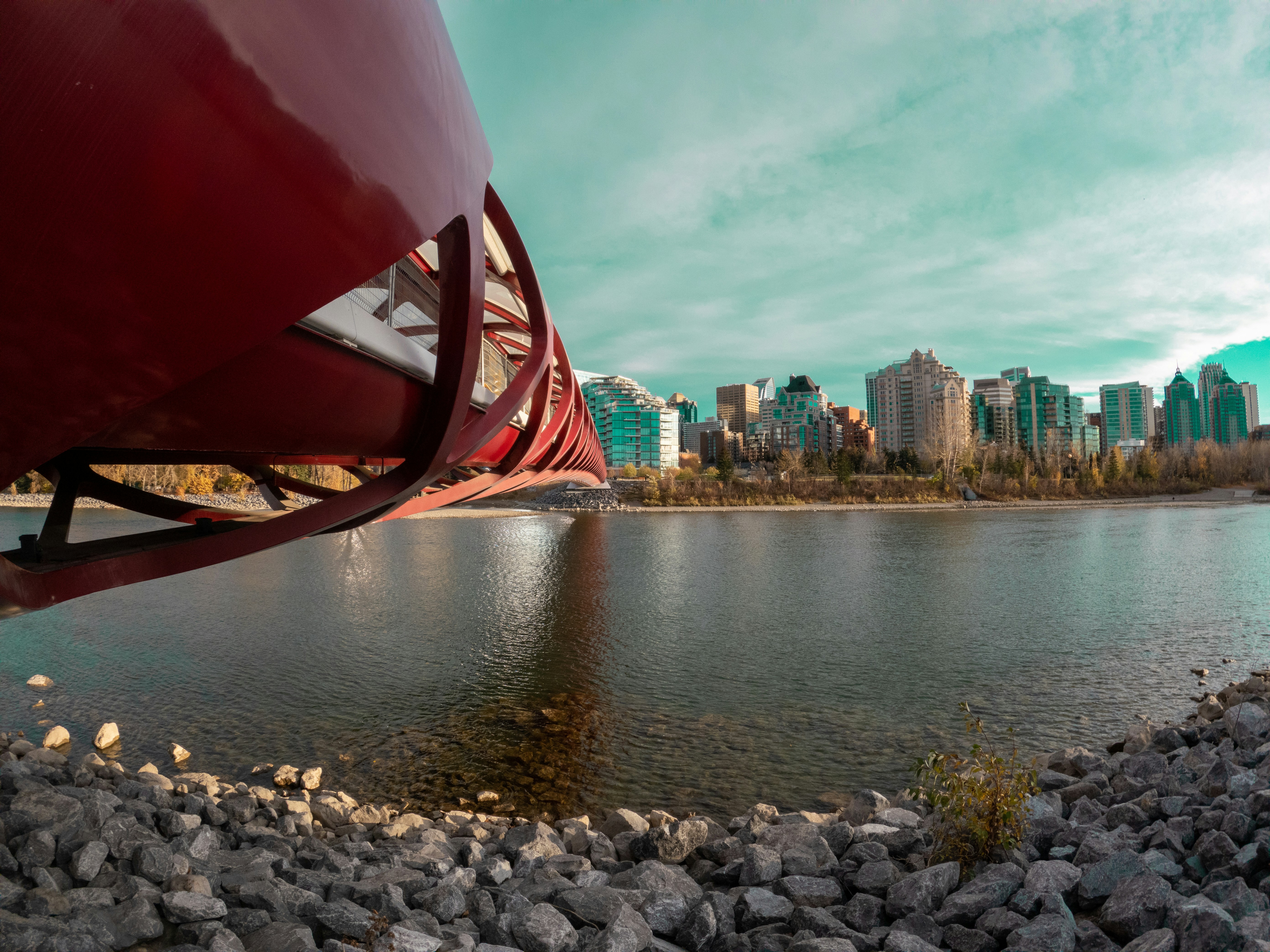 Ein rotes Metallobjekt an einem felsigen Ufer mit einer Stadt im Hintergrund