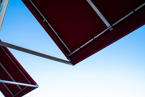 Metallic structures supporting a red fabric canopy against a clear blue sky.