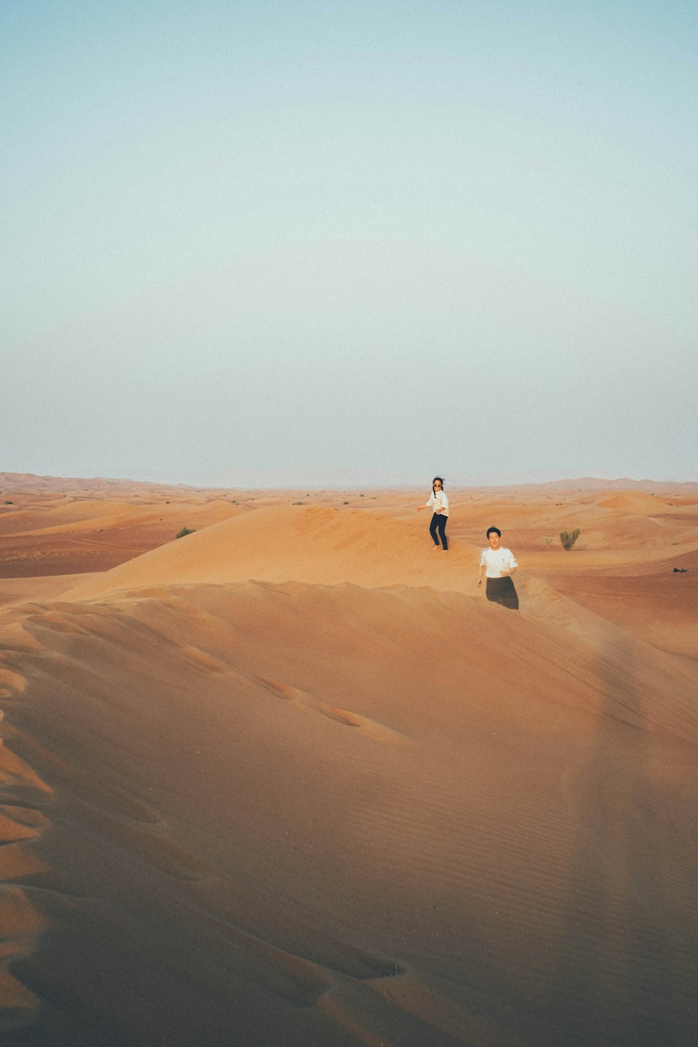 a couple of people walking in the desert with Wahiba Sands in the background
