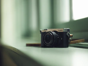 A sleek digital camera resting on a wooden table with soft natural light highlighting its lens.