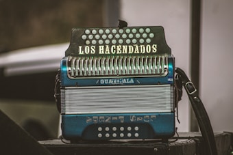 An accordion with the words 'LOS HACENDADOS' written on the keyboard section and 'GUATEMALA' on the body stands prominently. It features metallic buttons and a mix of blue and white colors. The background is slightly blurred, highlighting the instrument.