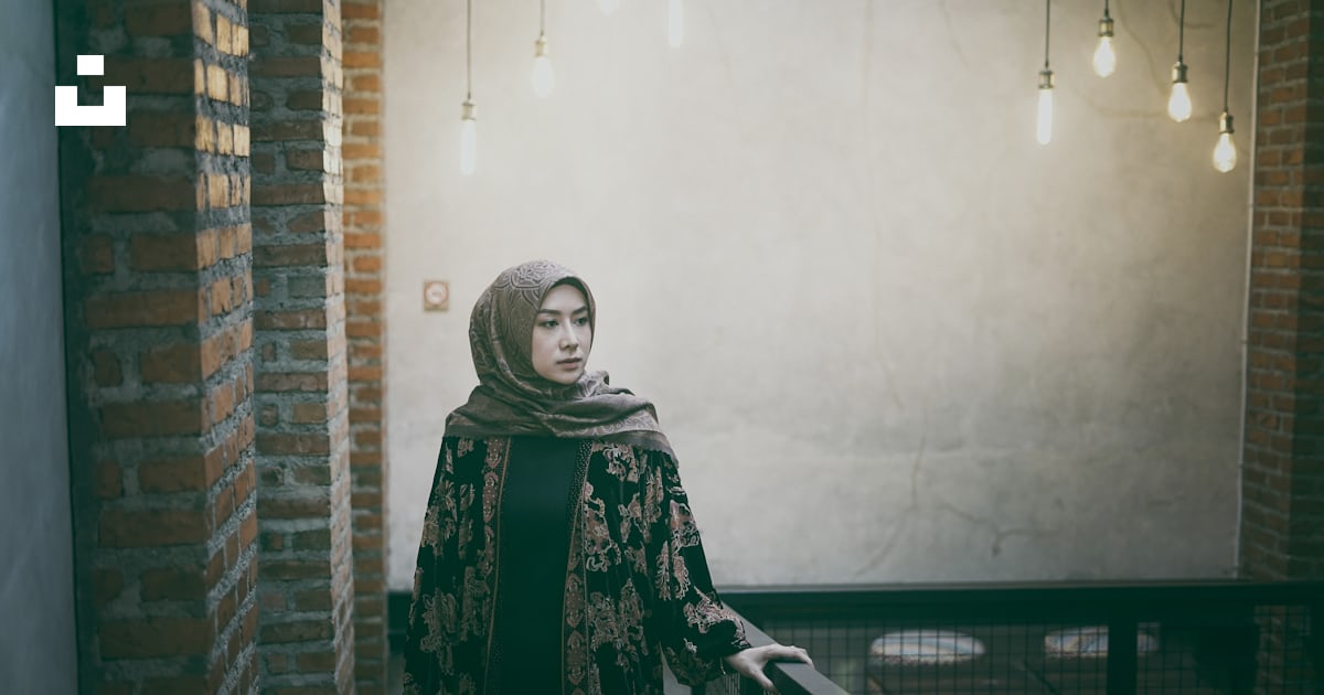 A woman in a green scarf and head scarf standing by a railing photo ...