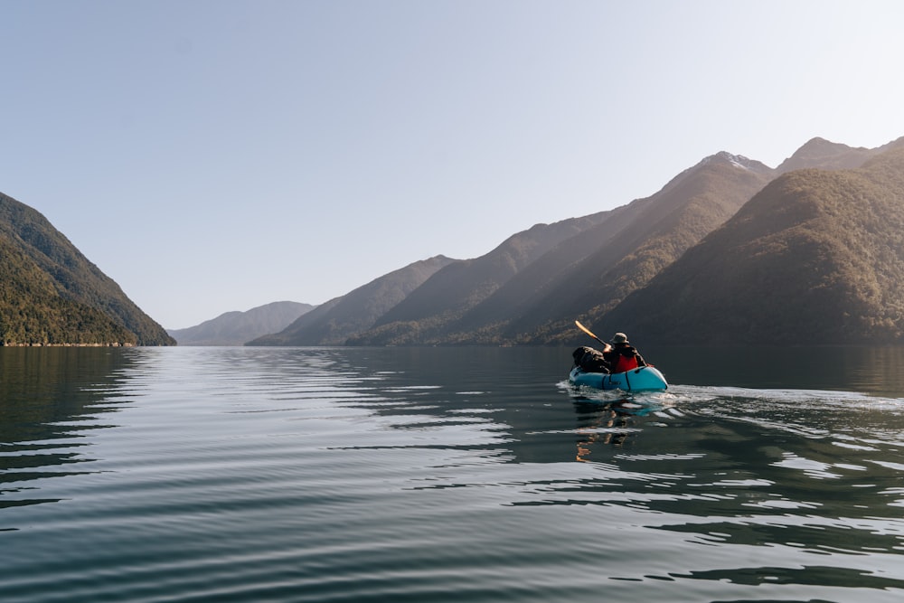 a couple people in a canoe on a lake with mountains in the background