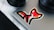 A laptop with a colorful fox sticker on it, positioned on a white wooden surface. Nearby are parts of a camera lens and a circular speaker.