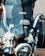 A close-up view of a motorcycle's chrome handlebars and windshield. Behind the windshield, a backpack with the word 'HOOKAH' is visible. The image captures the reflective surfaces and intricate mechanical details of the motorcycle.