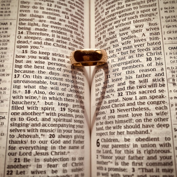 An open Bible with a gold ring placed on it, casting a heart-shaped shadow on the pages. The text is from Ephesians, focusing on themes related to love and wisdom.