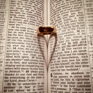 An open Bible with a gold ring placed on it, casting a heart-shaped shadow on the pages. The text is from Ephesians, focusing on themes related to love and wisdom.