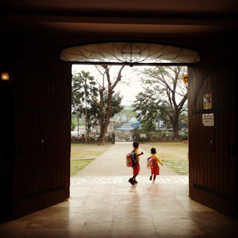 A calm and warm school entrance with parents and children walking together in the morning light.