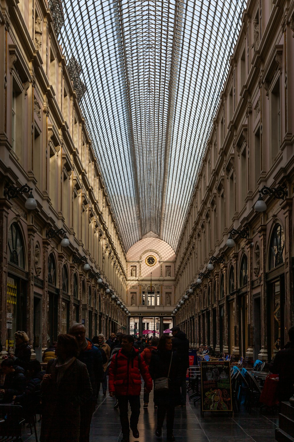 a group of people walking through a large building with many windows