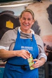 A smiling farmer holding fresh curd jars in a clean, green farm setting.