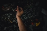 A hand is adjusting controls on an intricate panel filled with numerous dials and gauges, indicating a complex and technical environment.