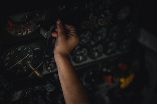 A hand is adjusting controls on an intricate panel filled with numerous dials and gauges, indicating a complex and technical environment.
