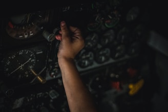 A hand is adjusting controls on an intricate panel filled with numerous dials and gauges, indicating a complex and technical environment.