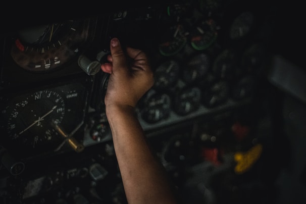 A hand is adjusting controls on an intricate panel filled with numerous dials and gauges, indicating a complex and technical environment.