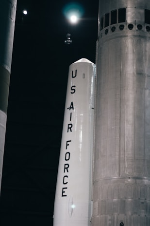 Team members in dark uniforms gathered around a launchpad model, discussing final adjustments under soft spotlight