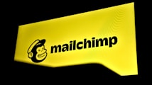 A bright yellow sign displaying the Mailchimp logo with a cartoon monkey face wearing a hat next to the brand name in bold black letters.