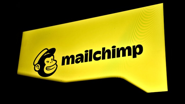 A bright yellow sign displaying the Mailchimp logo with a cartoon monkey face wearing a hat next to the brand name in bold black letters.