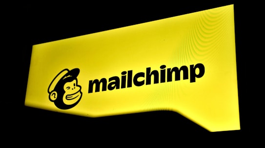 A bright yellow sign displaying the Mailchimp logo with a cartoon monkey face wearing a hat next to the brand name in bold black letters.