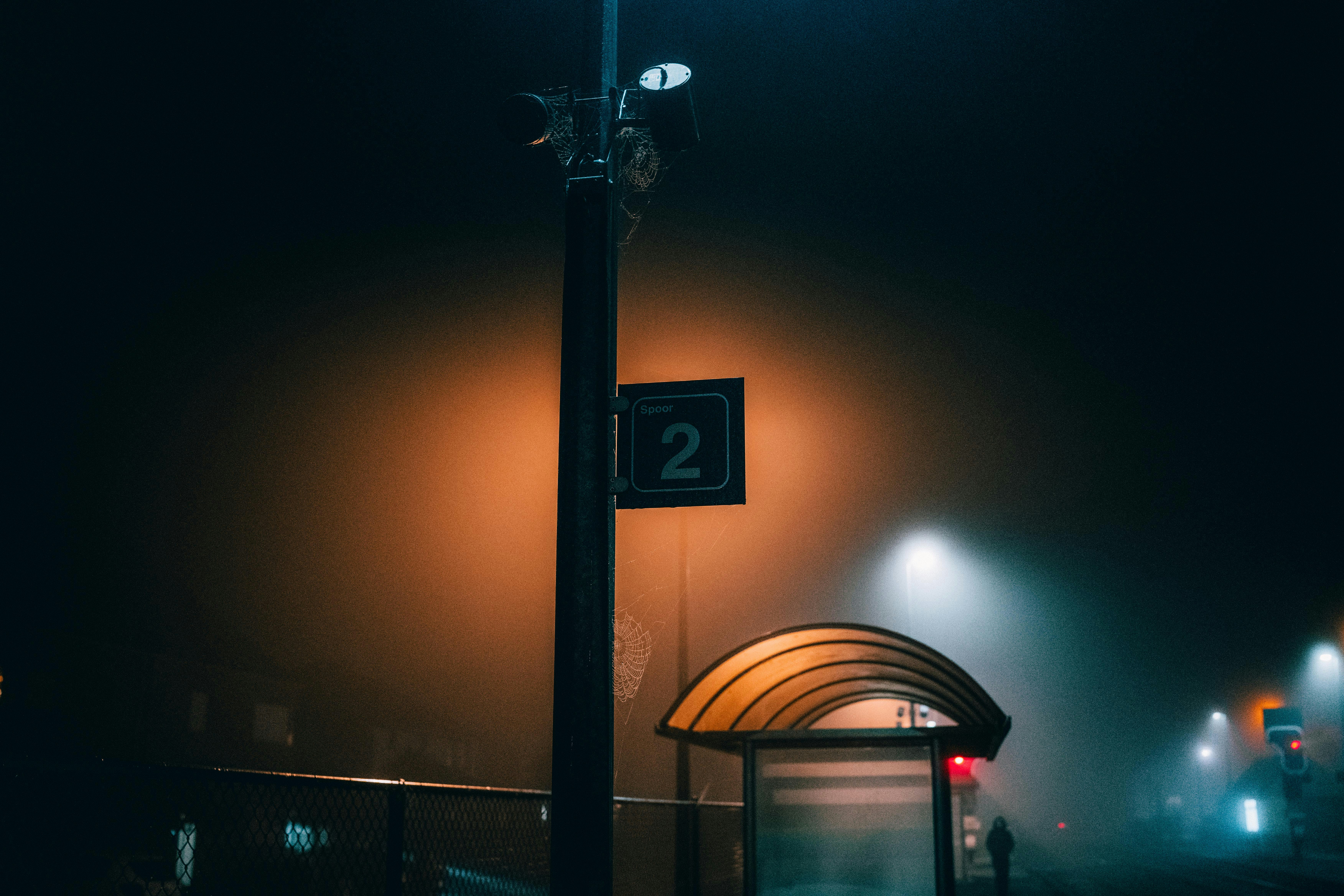 A fog-covered train station at dawn, a single lantern glowing through the mist, and an old bench beneath the sign that’s missing its name.