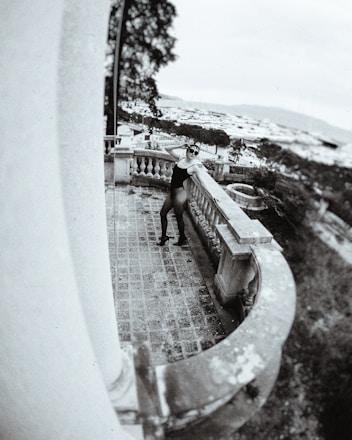 A stylish silhouette of an escort standing confidently by a city hotel balcony at dusk.