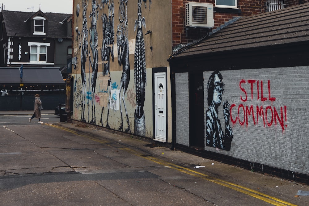 a person walking on a sidewalk next to a wall with graffiti