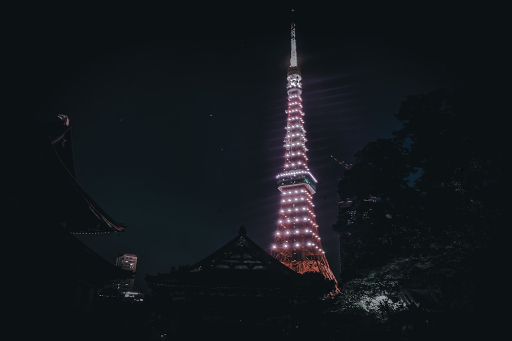 una torre alta iluminada por la noche con la Torre de Tokio al fondo