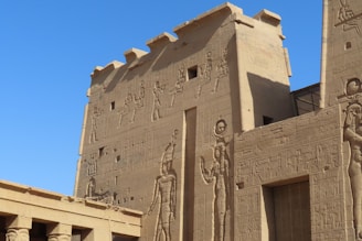 Ancient stone structures adorned with intricate carvings and hieroglyphics extending across large walls, depicting figures and symbols from a historical civilization.