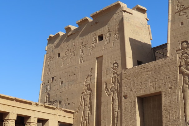 Ancient stone structures adorned with intricate carvings and hieroglyphics extending across large walls, depicting figures and symbols from a historical civilization.