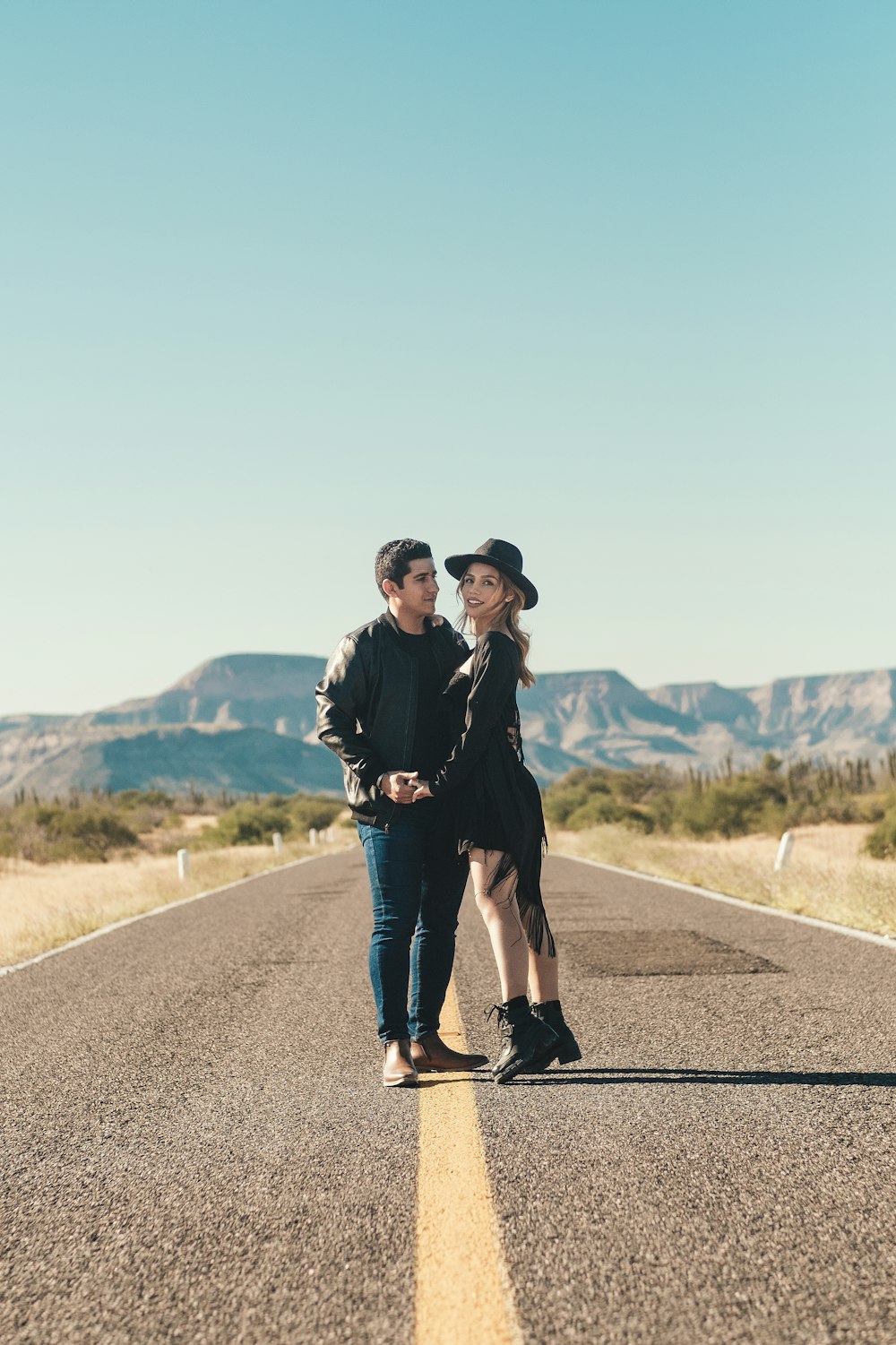 a man and woman standing on a road with mountains in the background