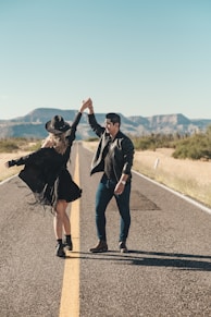 a man and woman standing on a road with a man in a hat and a cape with a