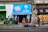 A small convenience store with a bright blue sign above the entrance displays 'Nestlé Savory' and 'confitería Castillo.' People are walking by or standing outside on the sidewalk. The storefront is surrounded by colorful graffiti and urban art. There are several backpacks and bags laid out on the pavement in front of the store.