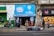 A small convenience store with a bright blue sign above the entrance displays 'Nestlé Savory' and 'confitería Castillo.' People are walking by or standing outside on the sidewalk. The storefront is surrounded by colorful graffiti and urban art. There are several backpacks and bags laid out on the pavement in front of the store.