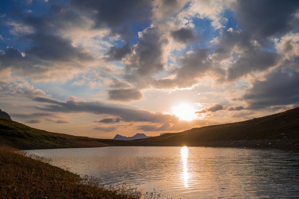 a body of water with hills and a sunset in the background