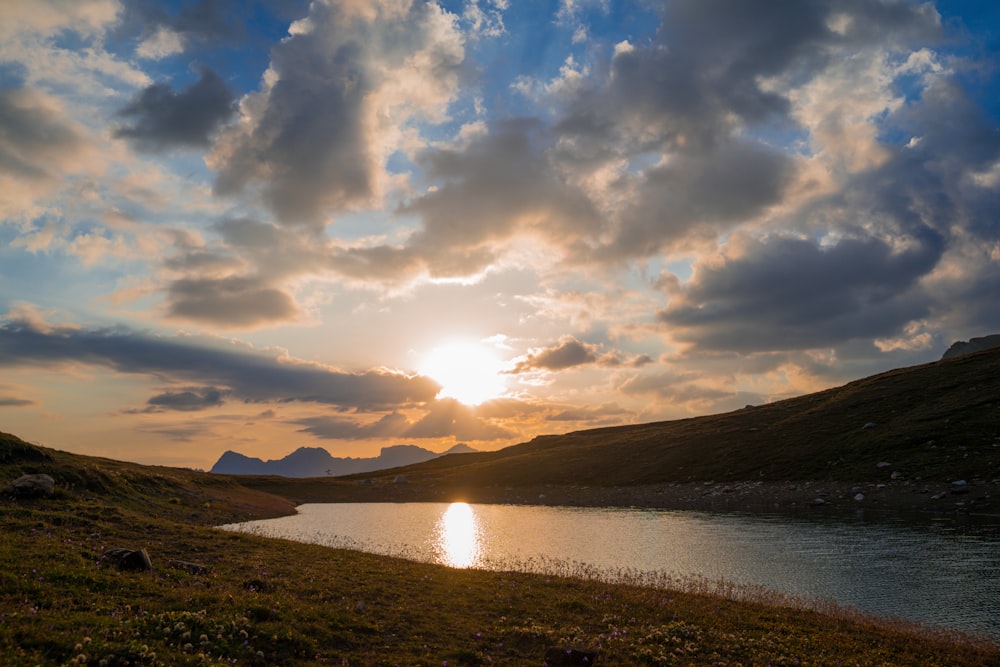 a body of water with hills around it and a cloudy sky above