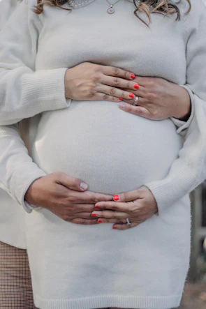 Close-up of hands supporting a pregnant belly, showing warmth and care in a cozy classroom setting