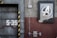 A detailed view of an industrial-style wall with a large emblem featuring a stylized letter 'A' within a circular frame, positioned on the right side. To the left, the number 'S-39' is prominently displayed on a metallic surface with black and yellow hazard stripes. Electrical panels and conduits run along the surface, contributing to the mechanical and utilitarian aesthetic.