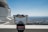 A public telescope is positioned in the foreground on a viewing platform, with a view of the expansive cityscape below. The sky is clear, creating an unobstructed view of the horizon. To the left, part of an observatory building is visible, featuring classic architectural details. A red notice on the telescope mentions a 'Covid 19 Alert'.