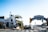 A sunny street view featuring the iconic Santa Monica Yacht Harbor sign, with palm trees and a lobster restaurant to the left. The intersection includes traffic lights and signs, along with some pedestrians in the background.