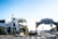 A sunny street view featuring the iconic Santa Monica Yacht Harbor sign, with palm trees and a lobster restaurant to the left. The intersection includes traffic lights and signs, along with some pedestrians in the background.