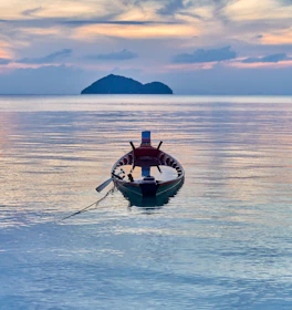 A sleek local boat anchored near Komodo Island at sunset with calm waters.