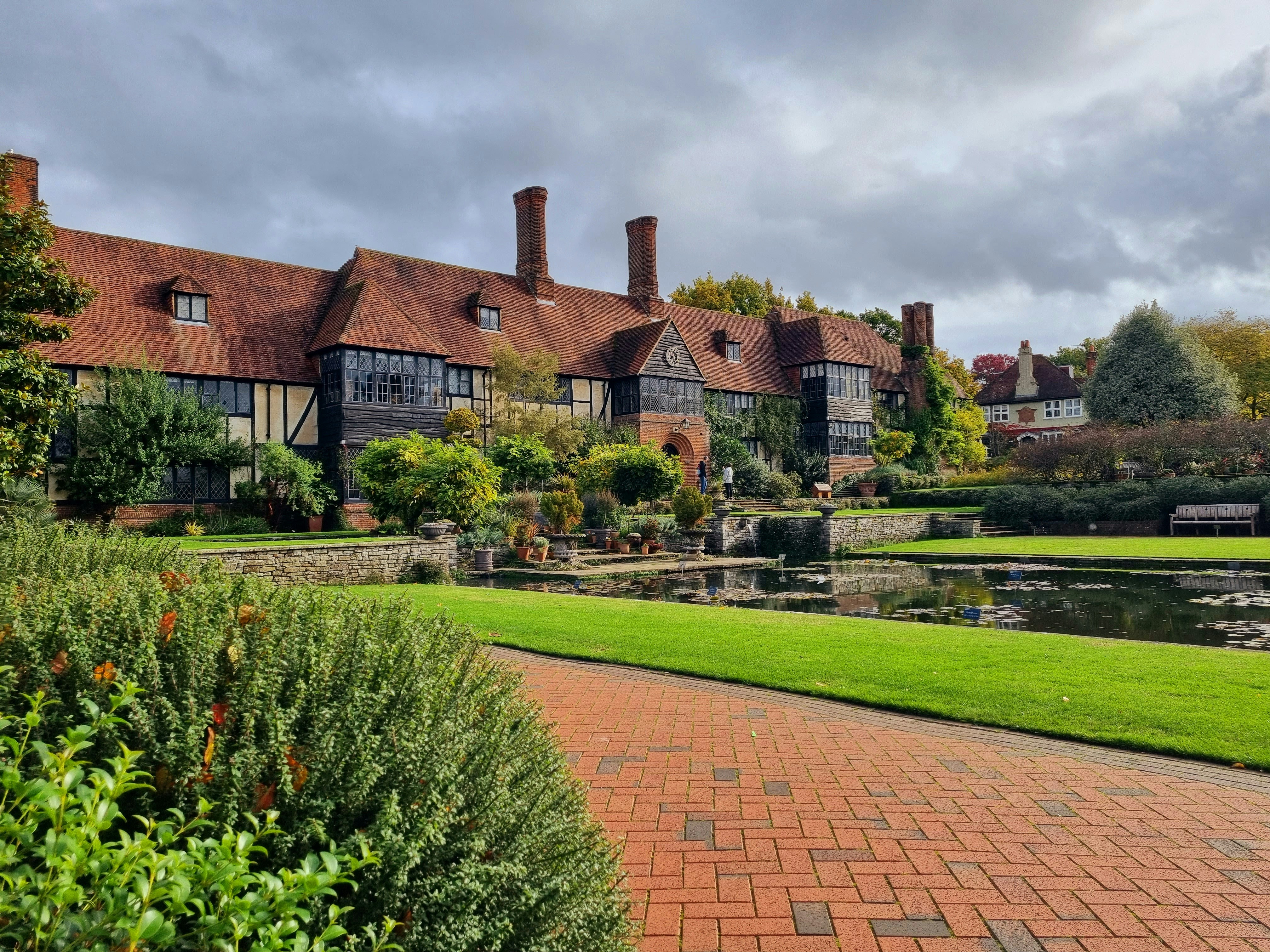 a brick path leading to a large house with a pond and a large lawn