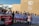 A diverse group of people are gathered outside a building with climate-related insignia. They are holding various banners with messages supporting human rights, indigenous rights, and anti-militarism. One banner reads 'DEFEND HUMAN RIGHTS AND THE RIGHTS OF INDIGENOUS PEOPLE,' and another reads 'MILITARISM POLLUTER COLONIZER.' A photographer is taking pictures of the group.