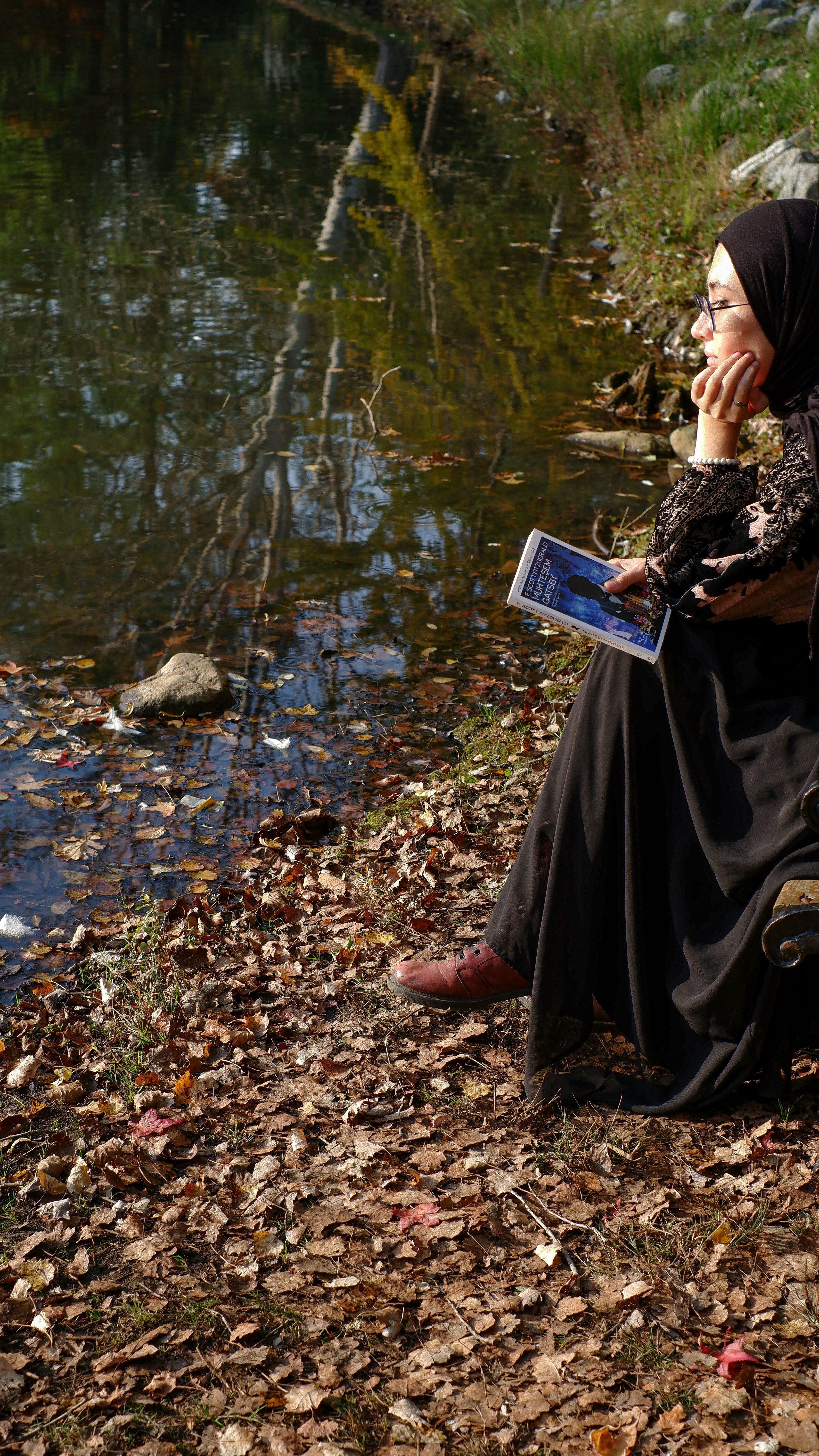 a person sitting on a rock reading a book by a river