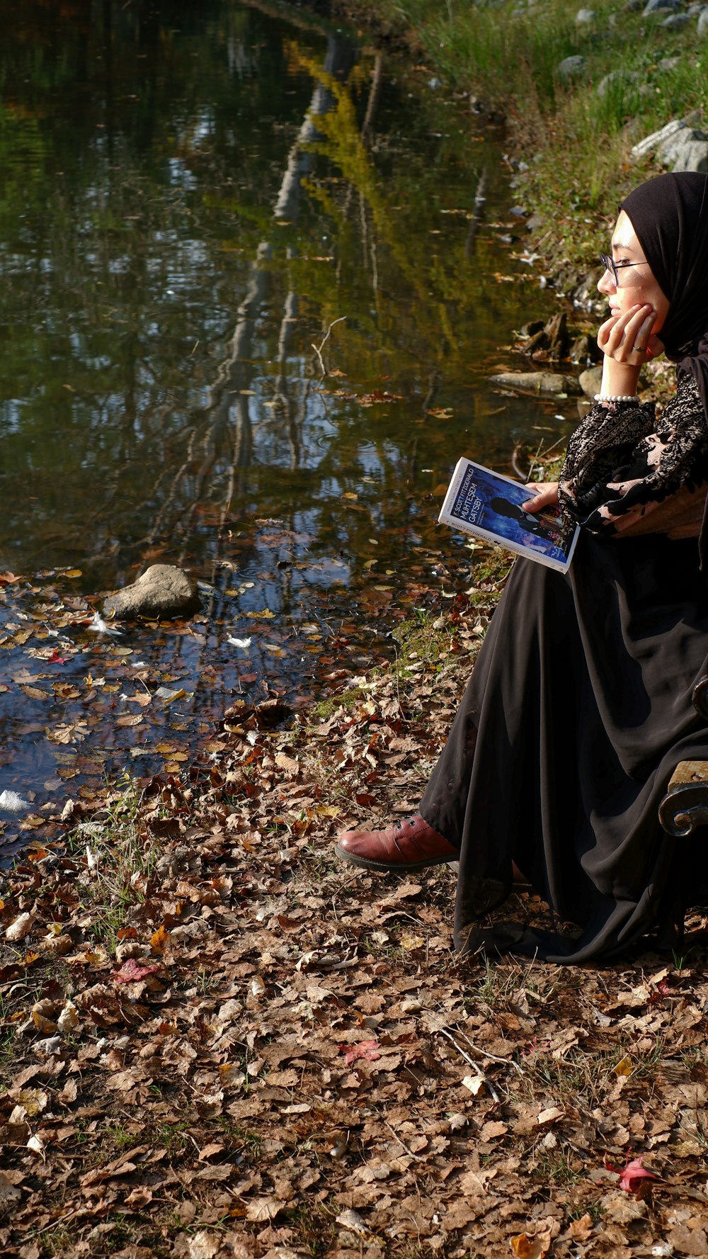 a person sitting on a rock reading a book by a river